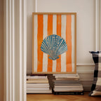a framed artwork of a seashell on a white wall, with a stack of books below it.