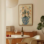 a cozy dining area with a table set for two, featuring a bottle of wine, a glass, and a vase of flowers. The table is surrounded by chairs, and a framed picture of flowers hangs on the wall above it.