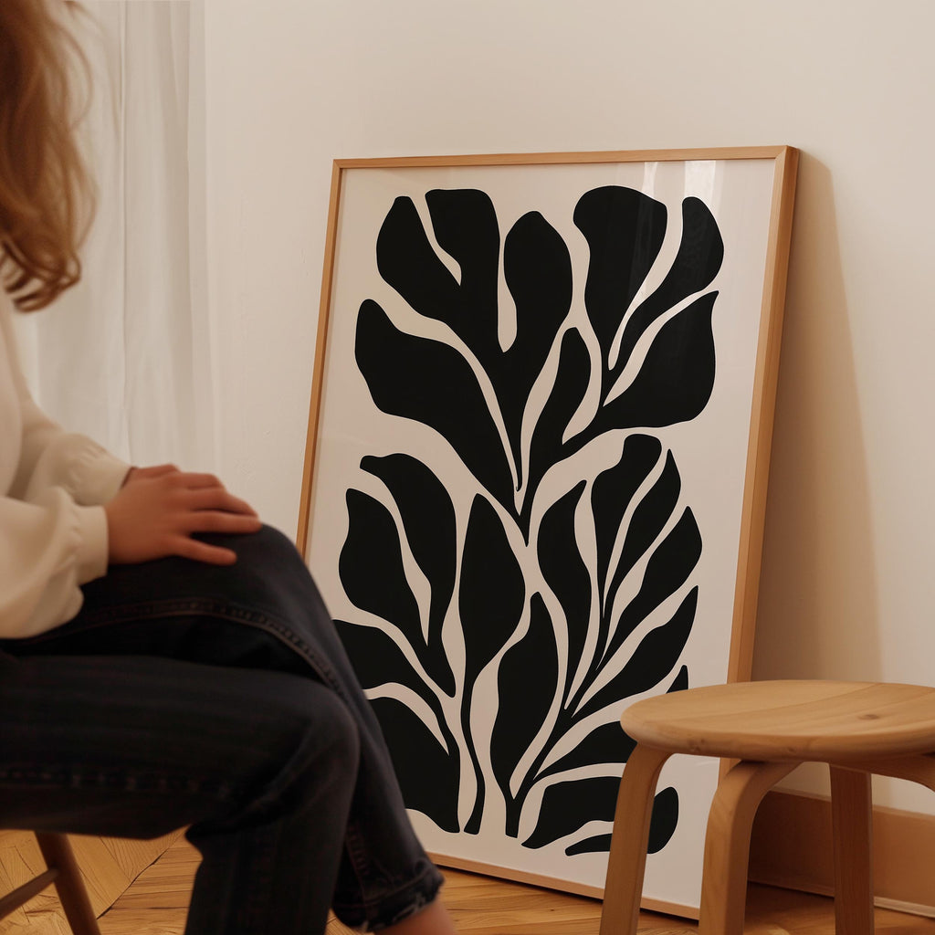 A person is sitting on a chair in front of a large framed artwork depicting a stylized black and white leaf design.