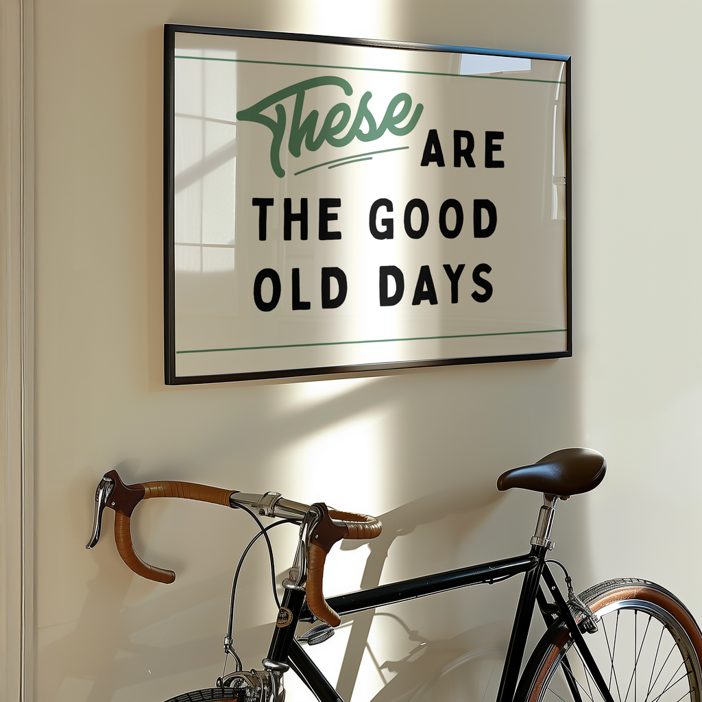 a framed sign with the text "These are the good old days" hanging on a wall next to a bicycle.