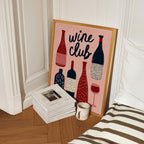 a framed poster with illustrations of wine bottles and glasses, placed on a wooden floor next to a stack of books and a coffee mug.