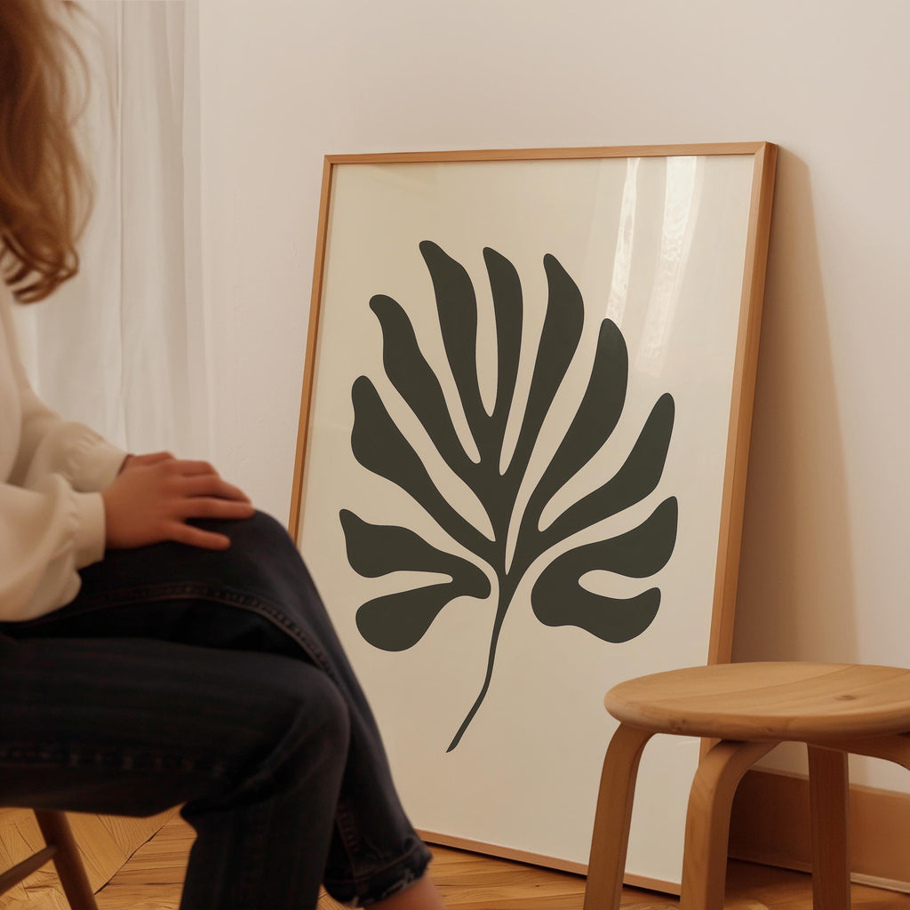 A person is sitting on a chair in front of a large framed artwork depicting a stylized leaf design.