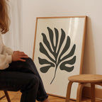A person is sitting on a chair in front of a large framed artwork depicting a stylized leaf design.