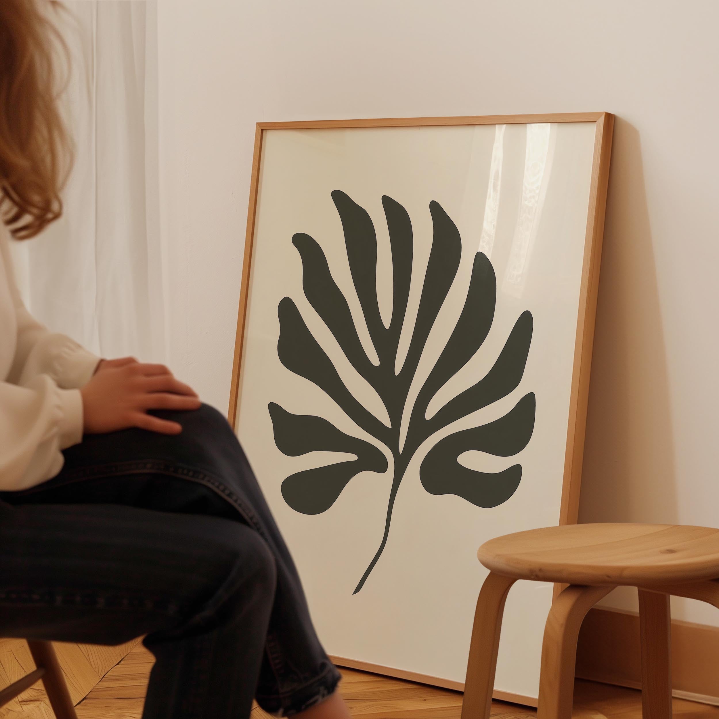 A person is sitting on a chair in front of a large framed artwork depicting a stylized leaf design.