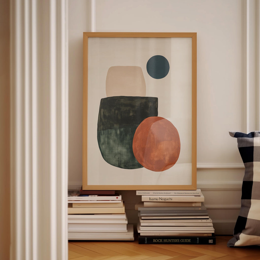 a framed abstract artwork with a large circle and two smaller circles, placed on a shelf among a stack of books.