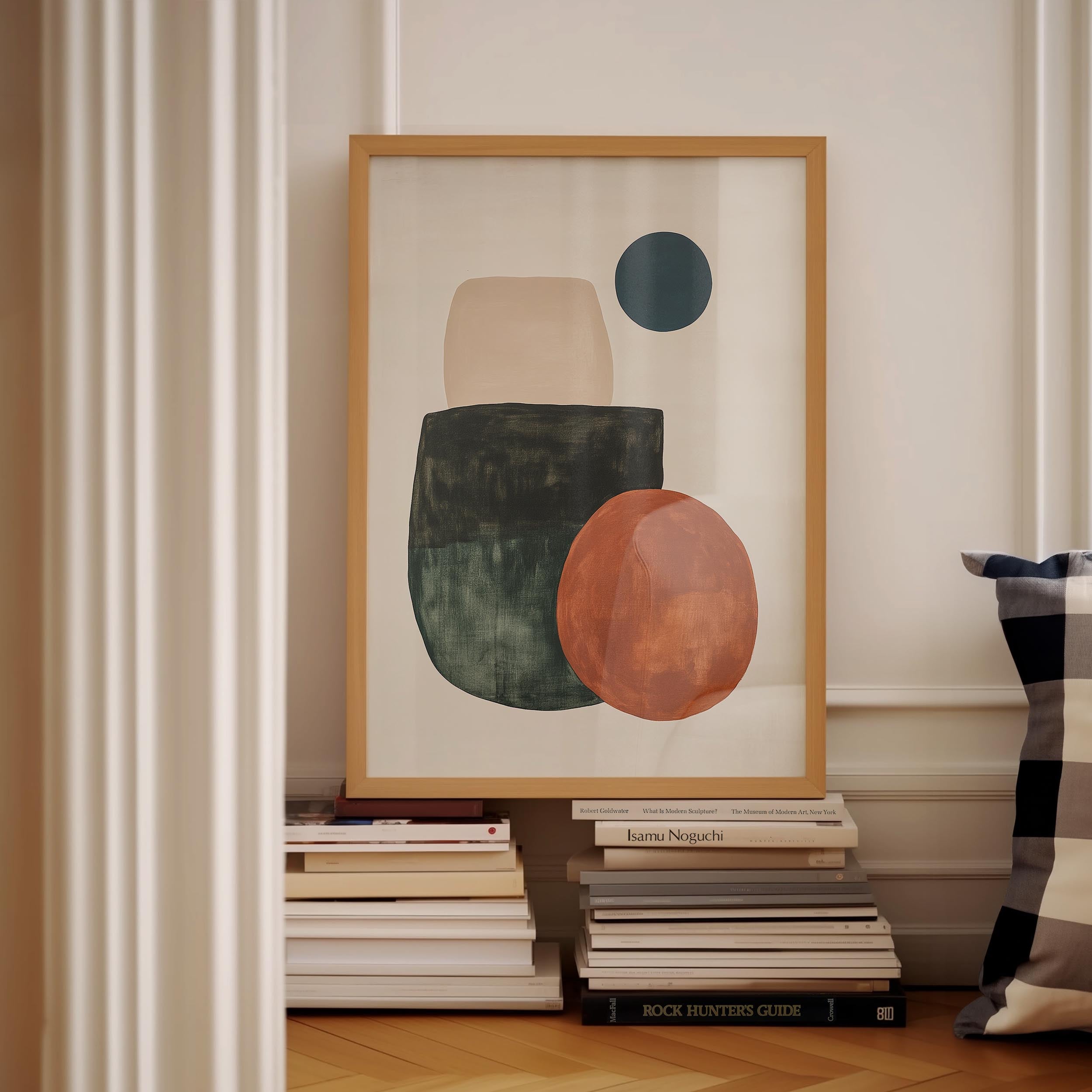 a framed abstract artwork with a large circle and two smaller circles, placed on a shelf among a stack of books.