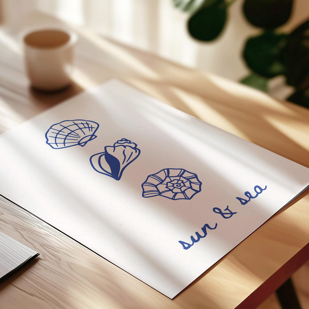 a white piece of paper with blue illustrations of seashells and the text "sun & sea" written on it, placed on a wooden surface.