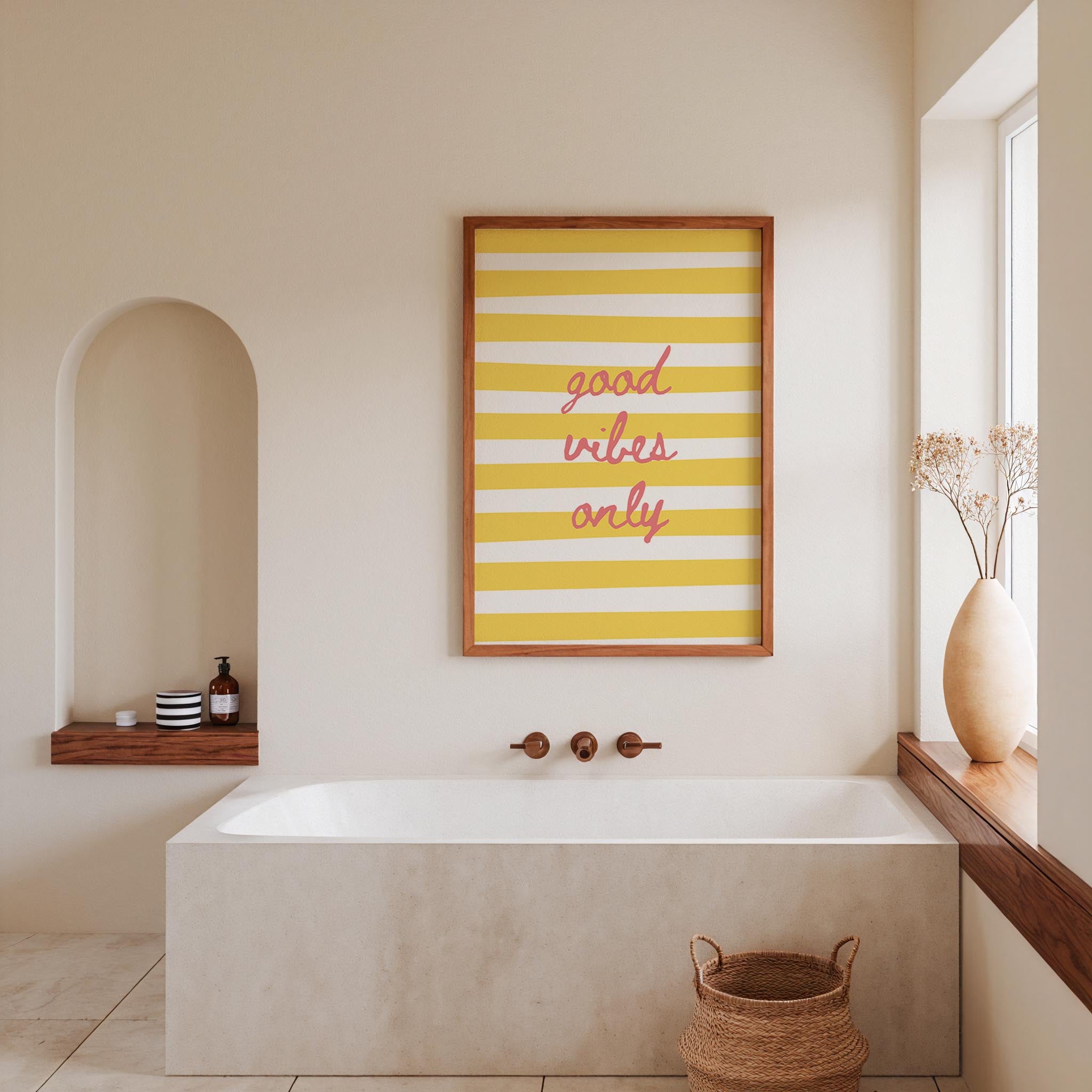 a bathroom with a white bathtub, a framed poster with the text "good vibes only" in the center, and a window with a vase of flowers on the sill.