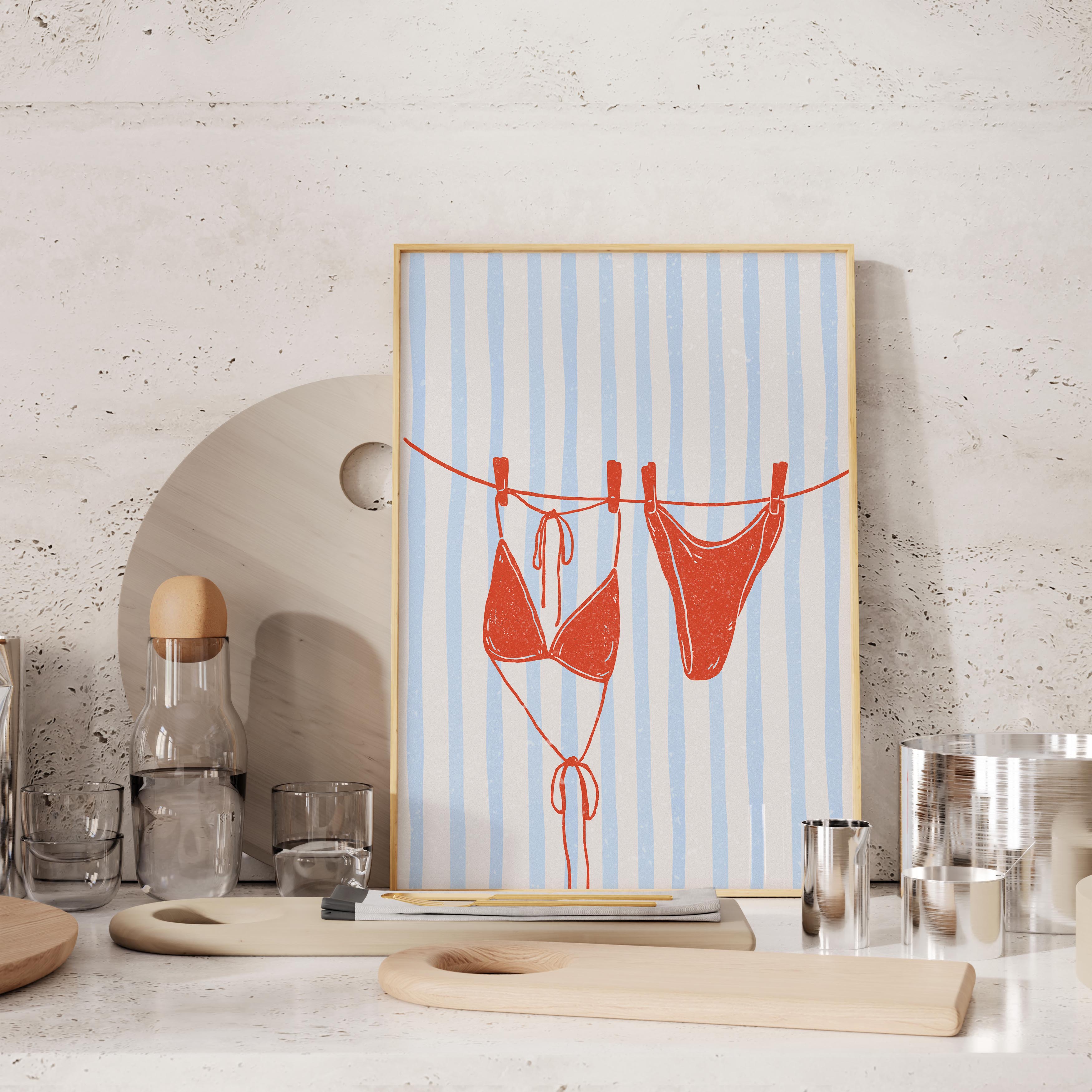 a framed artwork depicting a pair of red bikini bottoms hanging on a clothesline, with a blue and white striped background.