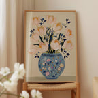 A framed painting of a vase filled with pink flowers is displayed on a wooden shelf.
