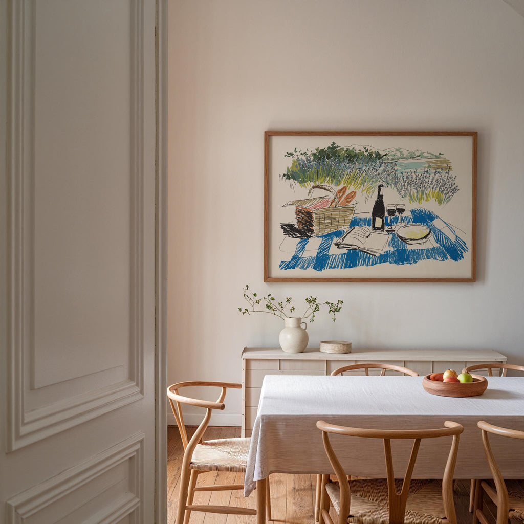 a cozy dining room with a white table and chairs, a vase of flowers, and a painting of a picnic scene on the wall.