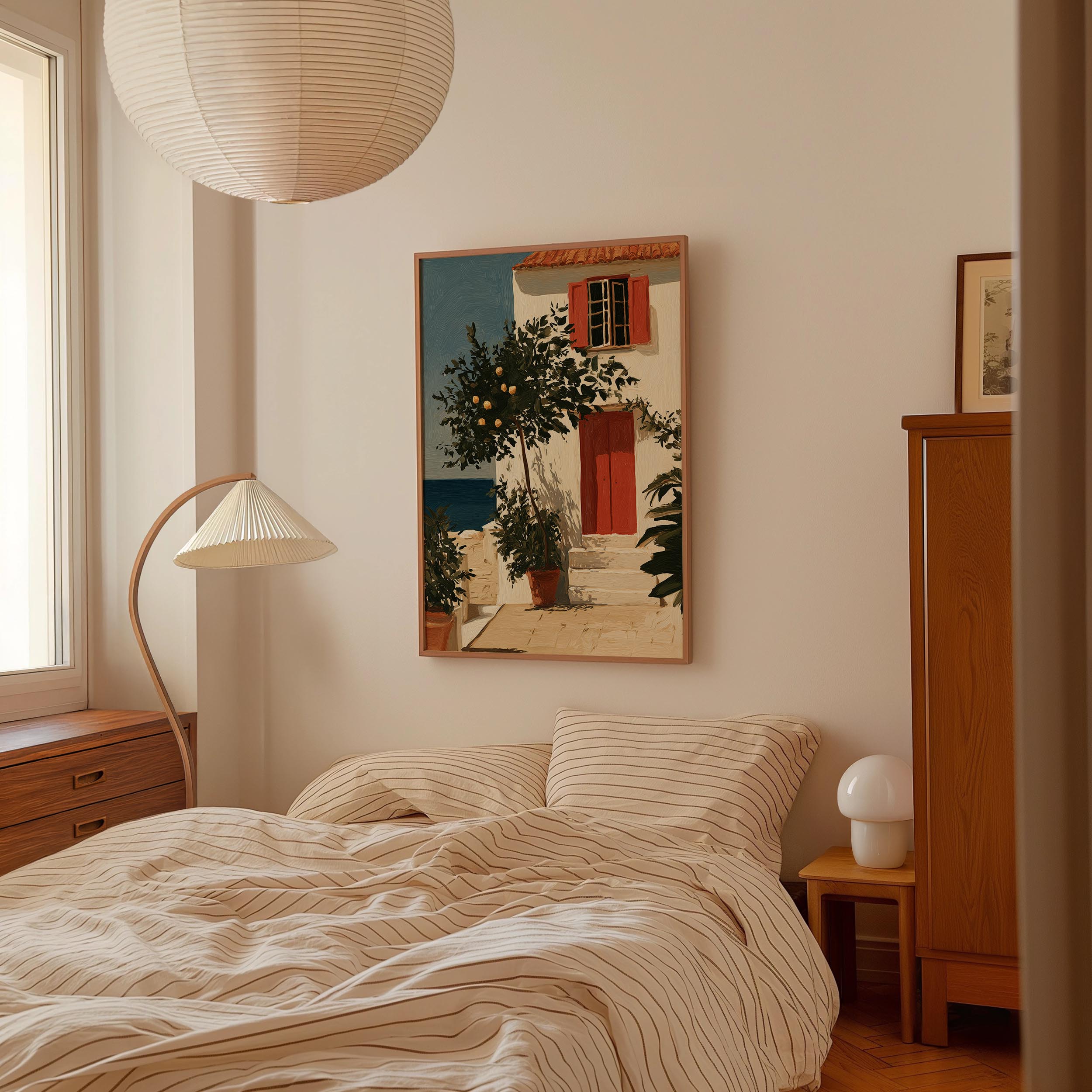 a cozy bedroom with a large bed, a wooden dresser, and a lamp. Above the bed is a framed painting of a house with a red door and a tree.