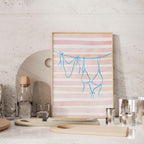 a framed artwork with a pink and white striped background, depicting a pair of blue underwear hanging on a clothesline. The artwork is displayed on a shelf, surrounded by various kitchen items such as a bottle, a glass, and a wooden cutting board.