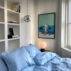 a cozy bedroom with a bed, a bookshelf, and a framed artwork on the wall.
