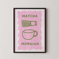 The image is a framed poster with a pink background and a green cup and whisk illustration. The text "MATCHA MORNING" is displayed above the illustration.