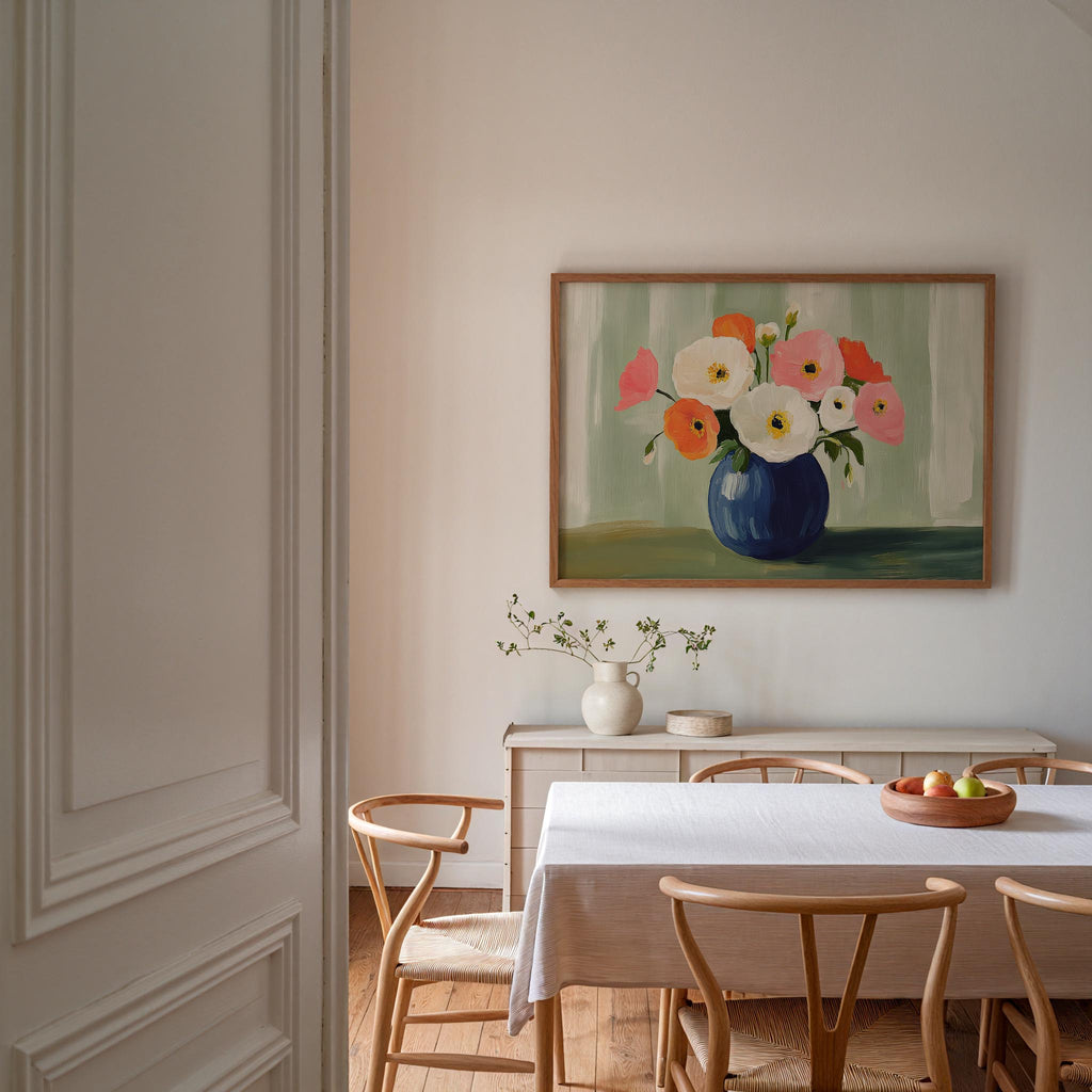 a dining room with a white table and chairs, a vase of flowers, and a painting of flowers hanging on the wall above the table.