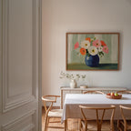 a dining room with a white table and chairs, a vase of flowers, and a painting of flowers hanging on the wall above the table.
