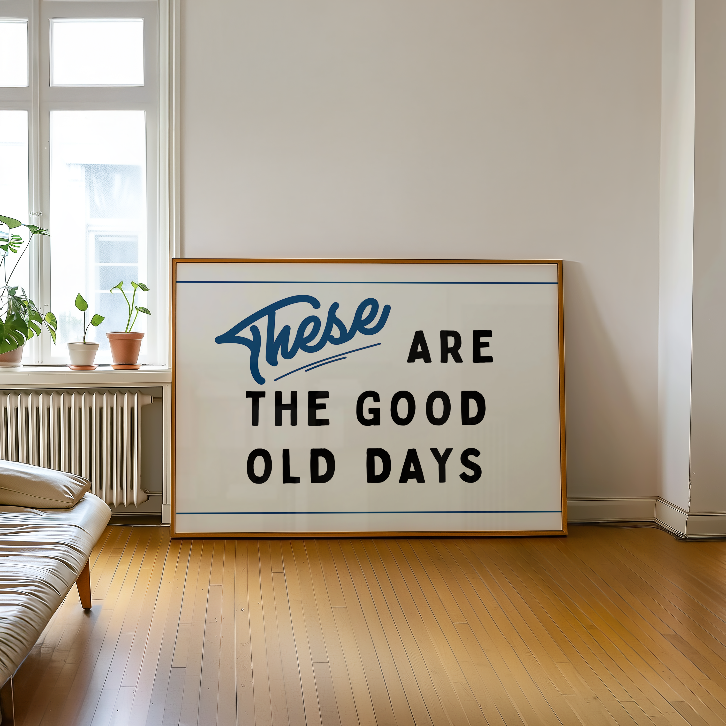 a large framed sign with the text "These are the good old days" on it, placed on a wooden floor in a room with a window and a plant.