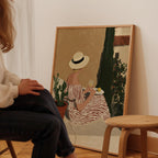A person is sitting in front of a painting that depicts a woman in a striped dress and hat, holding a glass of wine and a plate of food.