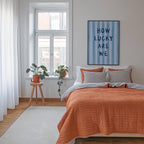 a cozy bedroom with a large bed, a wooden stool with a potted plant, and a framed poster on the wall.