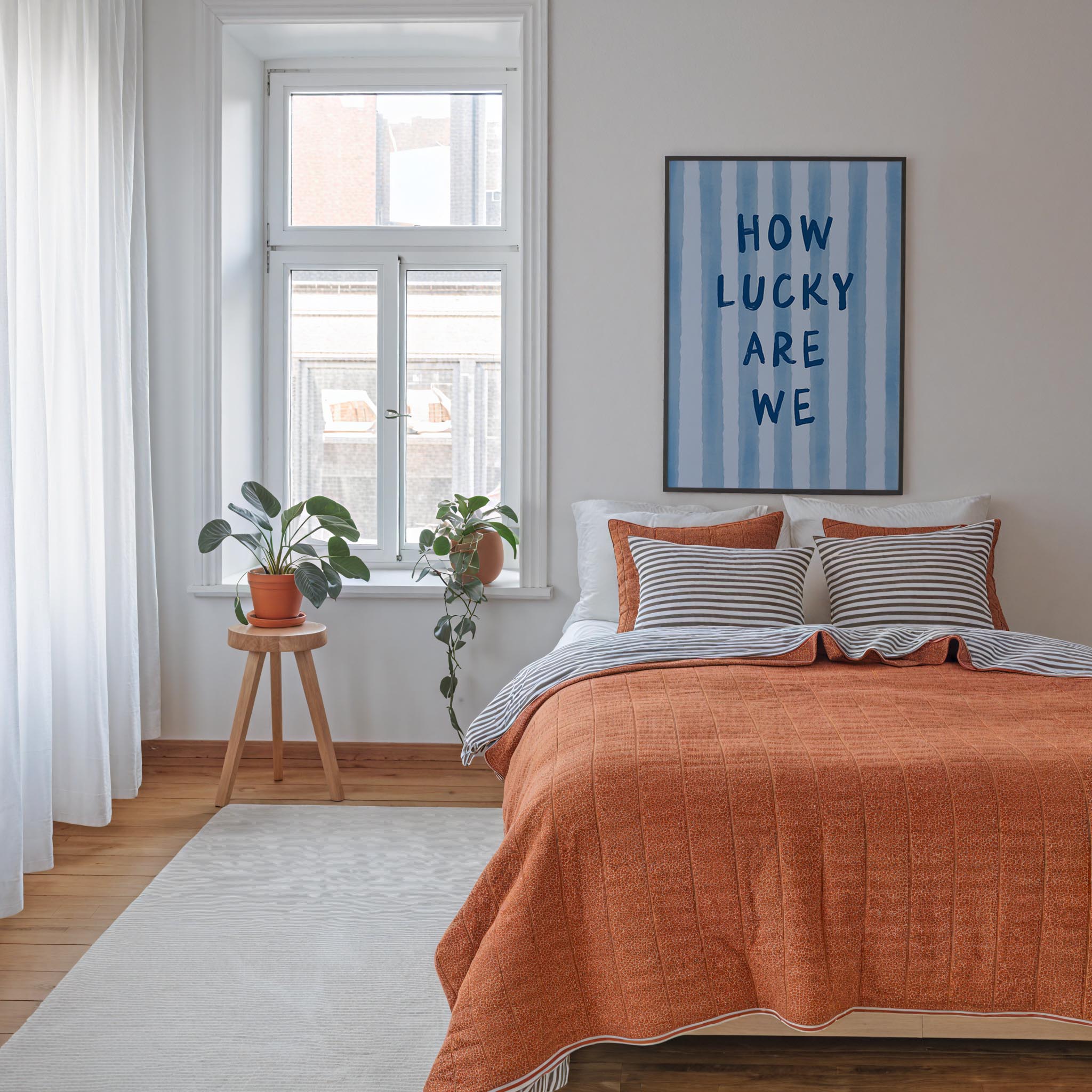 a cozy bedroom with a large bed, a wooden stool with a potted plant, and a framed poster on the wall.