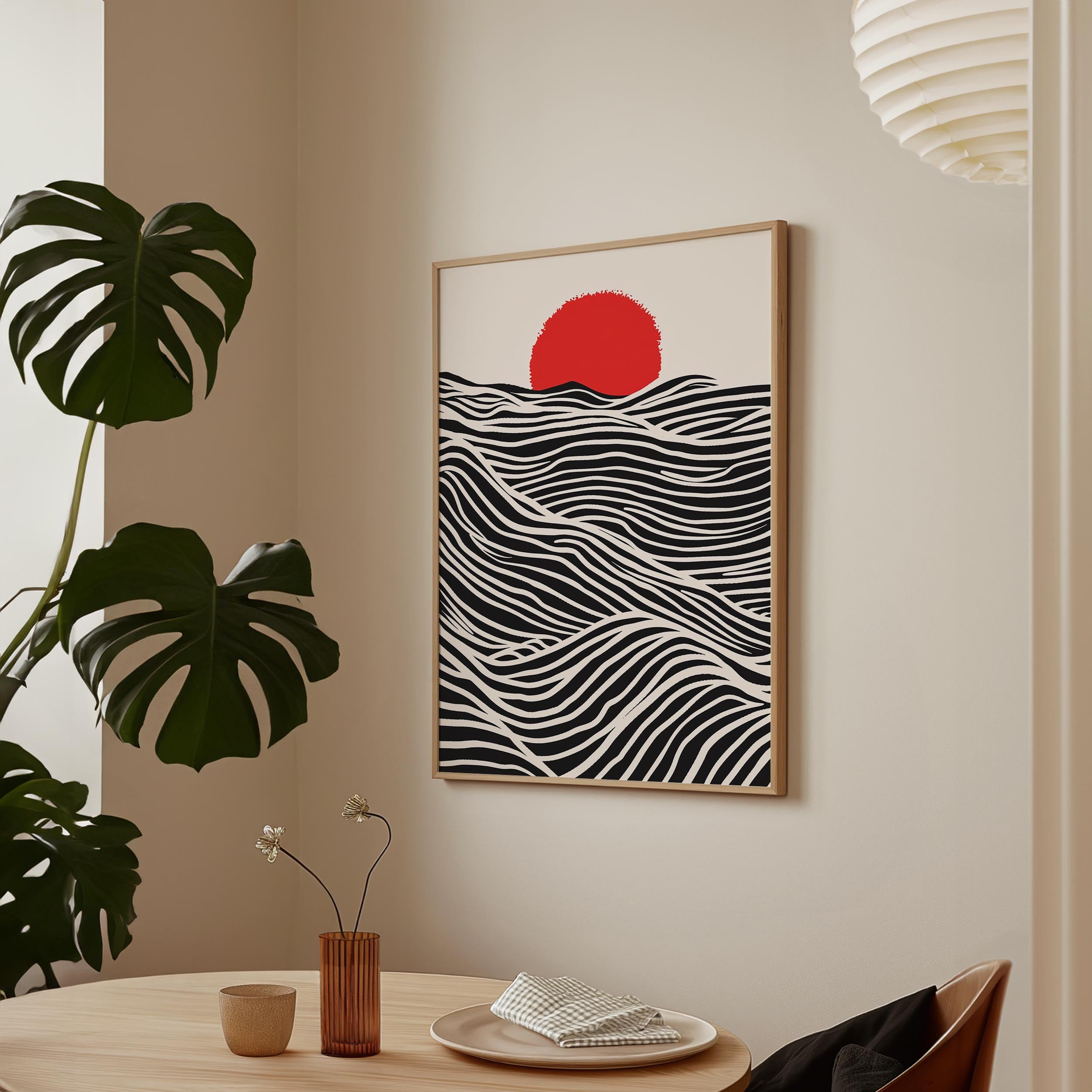 a minimalist dining area with a wooden table, a vase with flowers, and a framed artwork depicting a red sun on a black and white wave-like background.