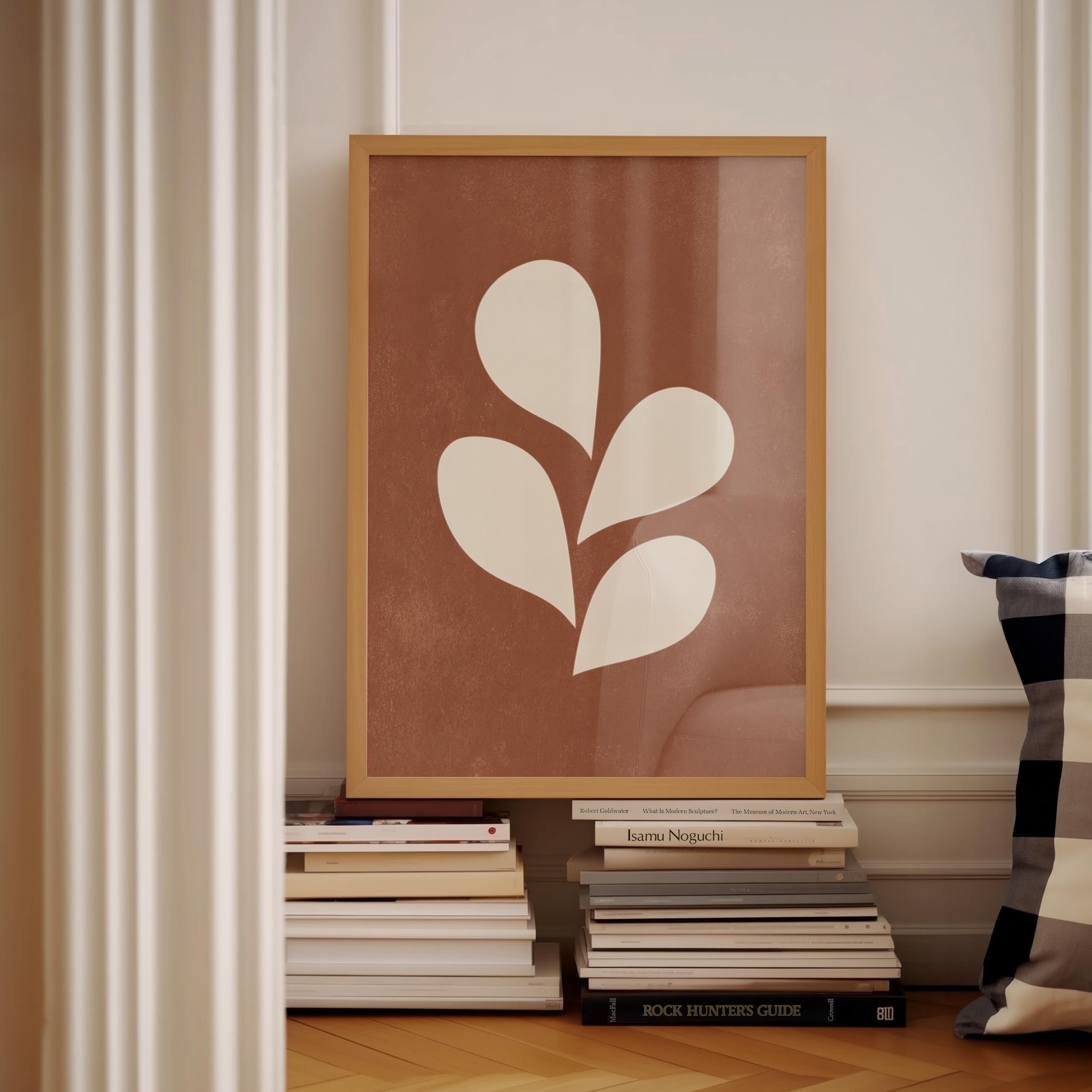 a framed artwork with a white leaf design, placed on a shelf among a stack of books.