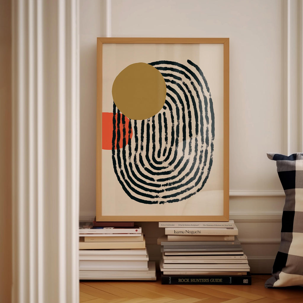 a framed abstract art piece with a black and white spiral design and a large yellow circle, displayed on a shelf among a stack of books.