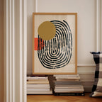 a framed abstract art piece with a black and white spiral design and a large yellow circle, displayed on a shelf among a stack of books.