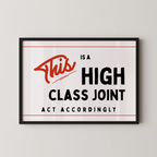 a framed sign with the text "This is a high class joint" in bold black letters, accompanied by a red cursive "This" symbol.