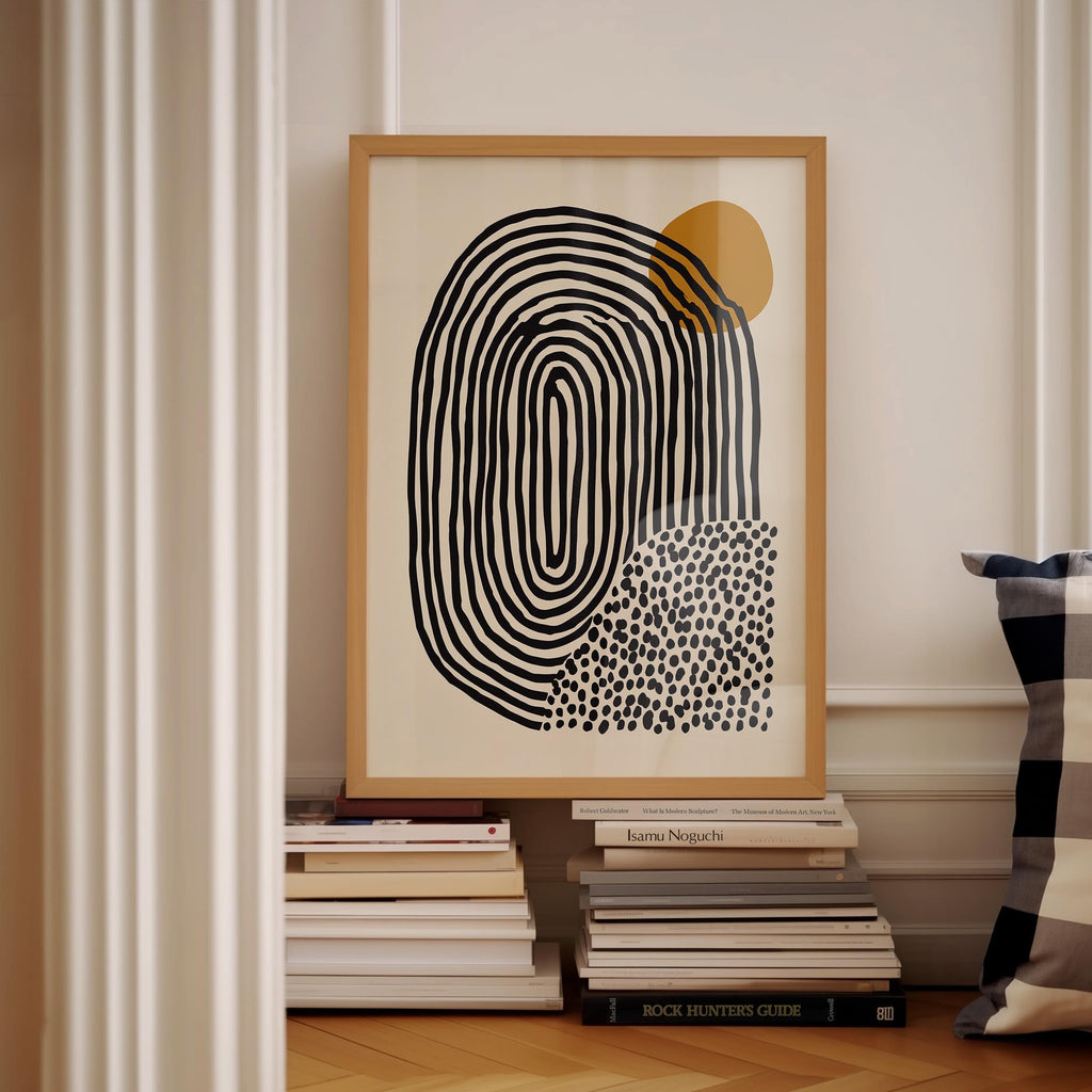 a framed abstract art piece with a black and white design, placed on a shelf next to a stack of books.