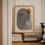 a framed abstract art piece with a black and white design, placed on a shelf next to a stack of books.