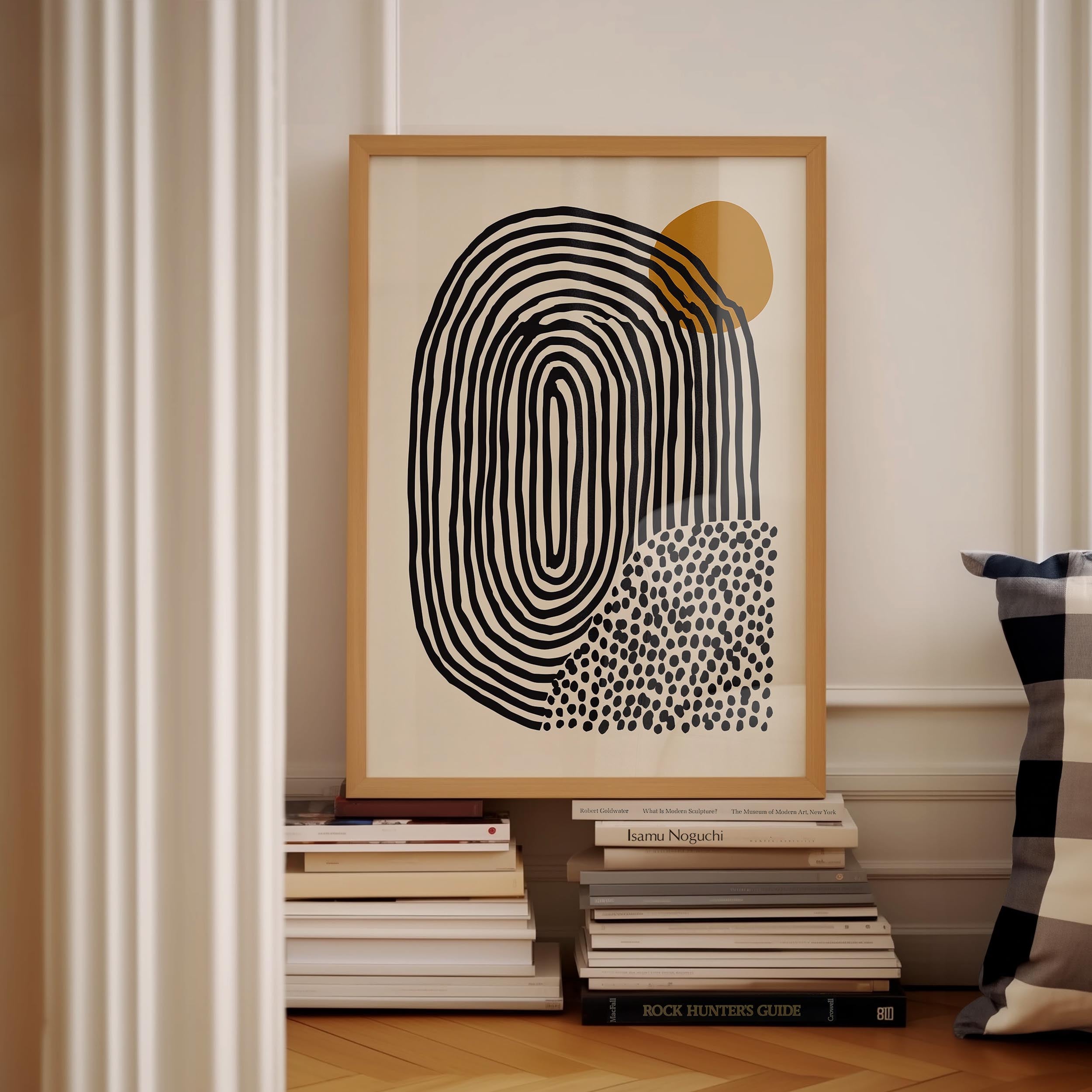 a framed abstract art piece with a black and white design, placed on a shelf next to a stack of books.