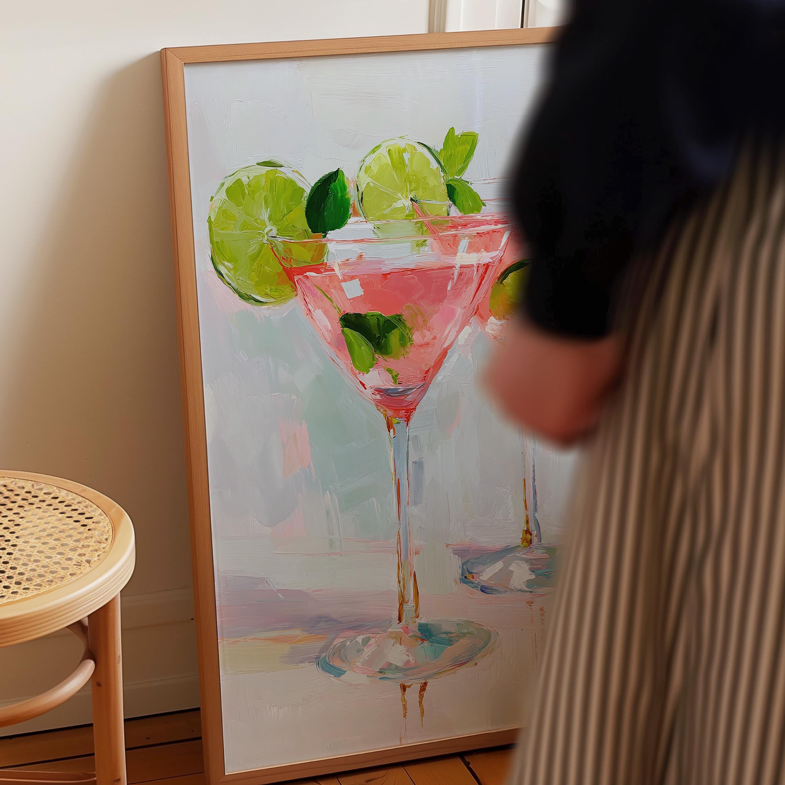 a painting of a pink cocktail glass with lime slices, displayed on a wall.