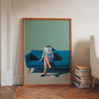A framed painting depicting a woman sitting on a blue couch, reading a book, with a stack of books next to her.