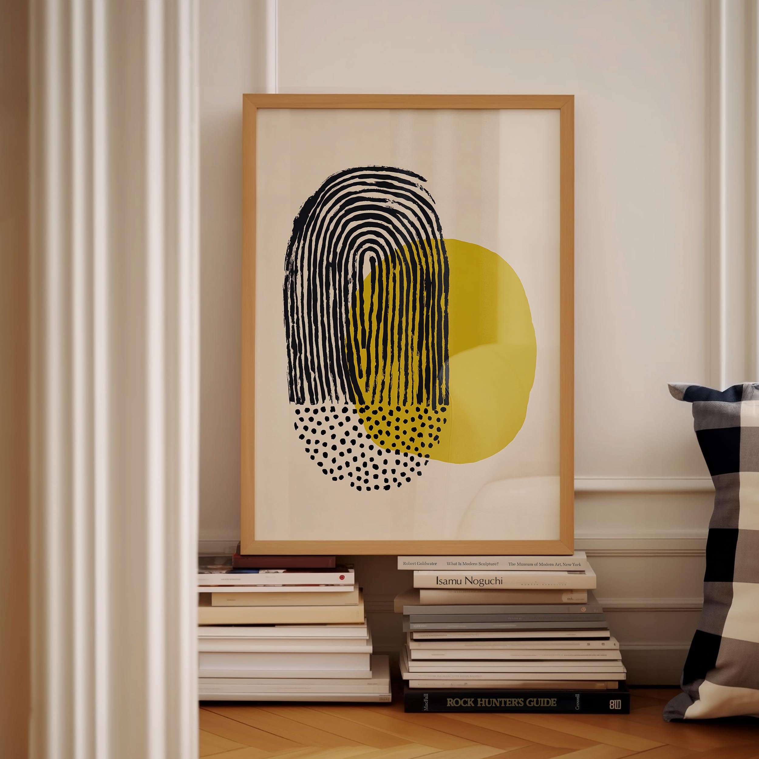 a framed abstract art piece with a black and yellow design, placed on a shelf next to a stack of books.