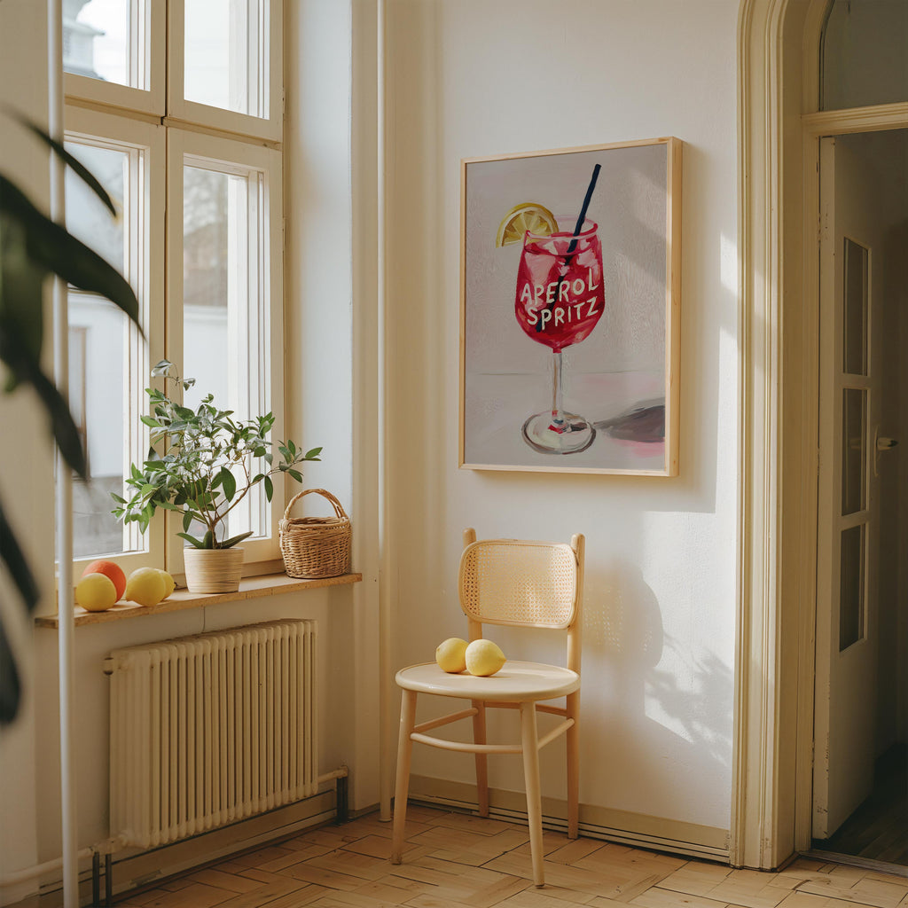 a cozy corner of a room with a wooden chair, a basket of fruit, and a framed picture of a glass of Aperol Spritz.