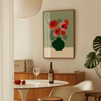 a dining room with a table, a wine bottle, a wine glass, and a framed picture of red flowers on the wall.