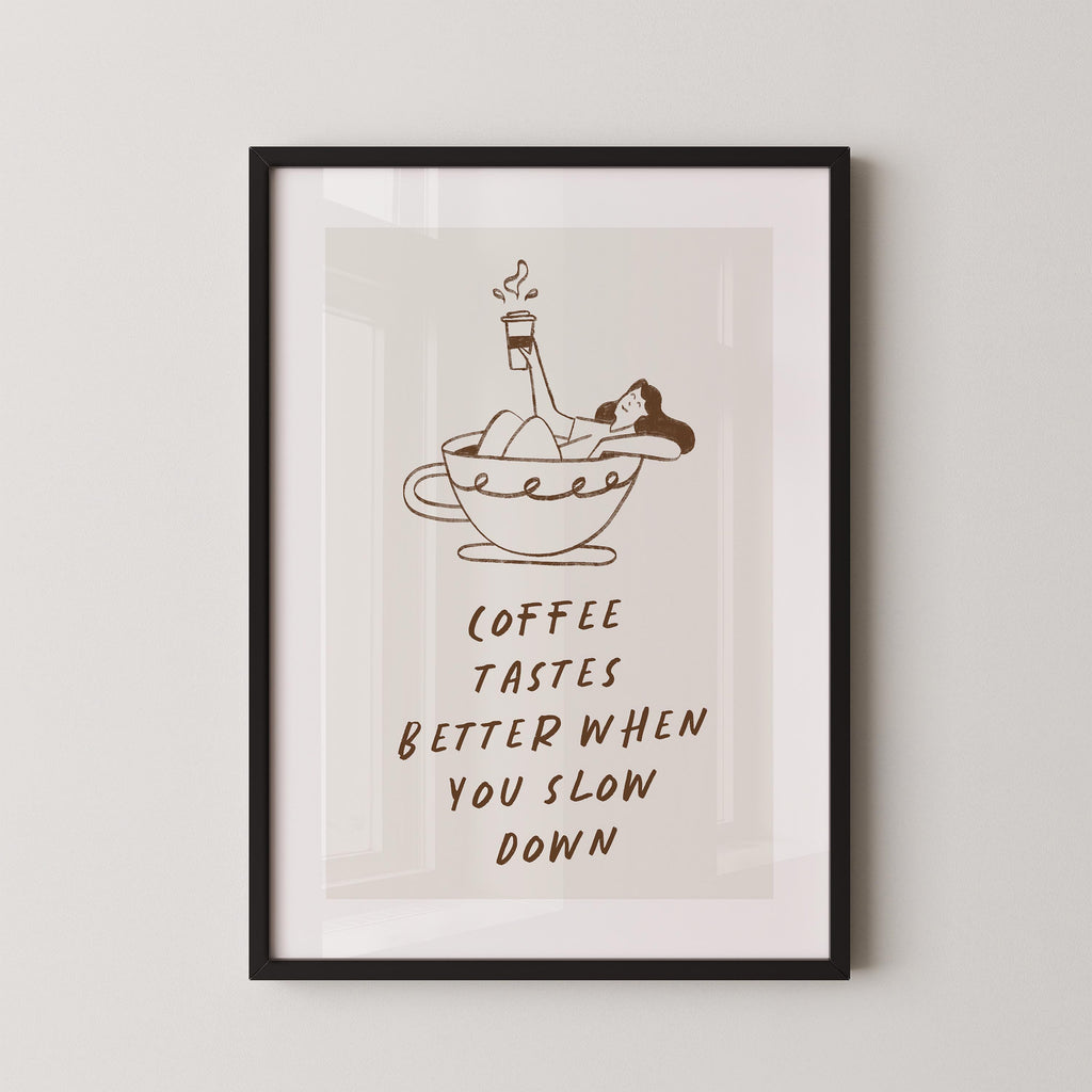 a framed poster with a cartoon illustration of a woman relaxing in a cup of coffee, accompanied by the text "Coffee tastes better when you slow down".