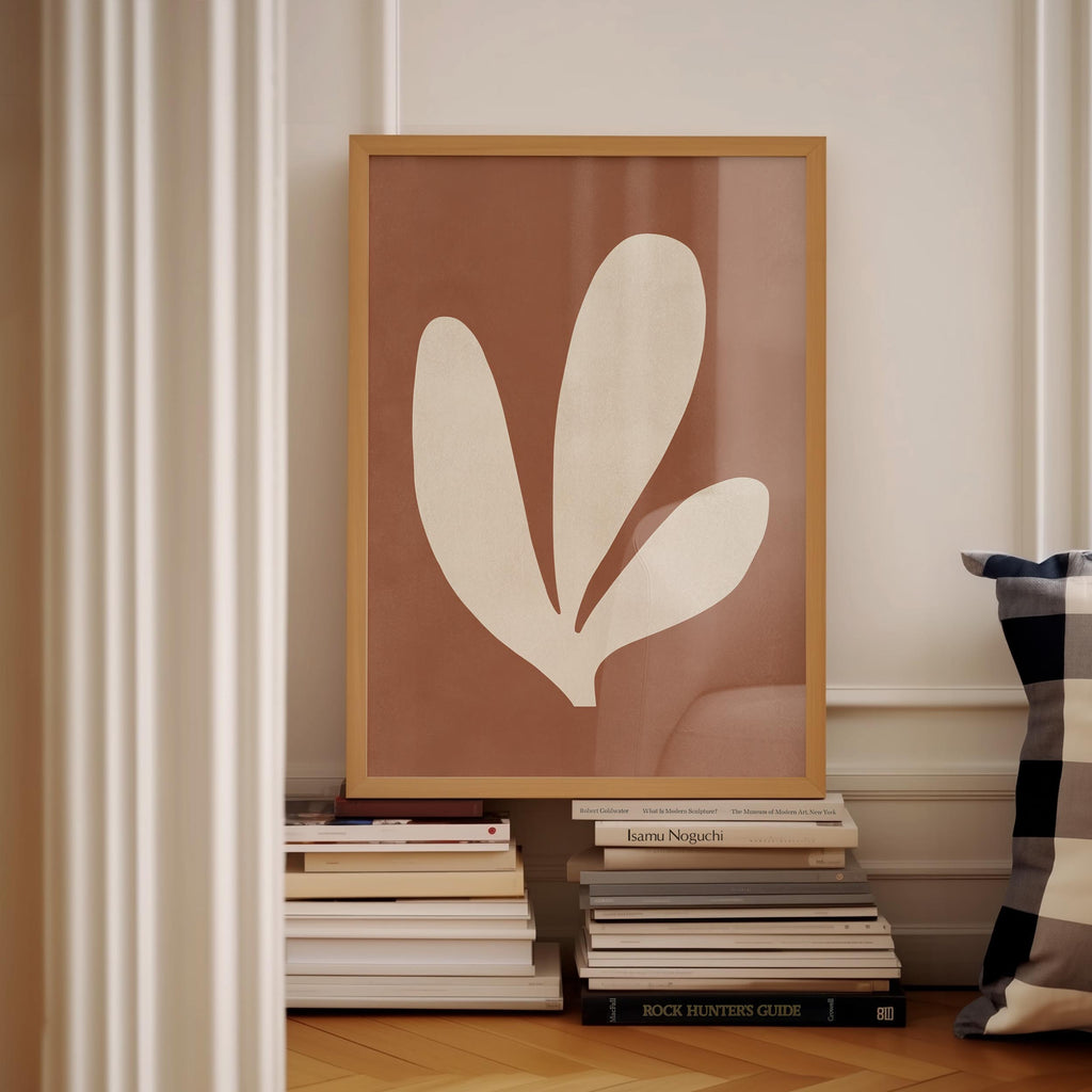 a framed artwork of a leaf-like shape, placed on a shelf among a stack of books.