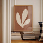 a framed artwork of a leaf-like shape, placed on a shelf among a stack of books.