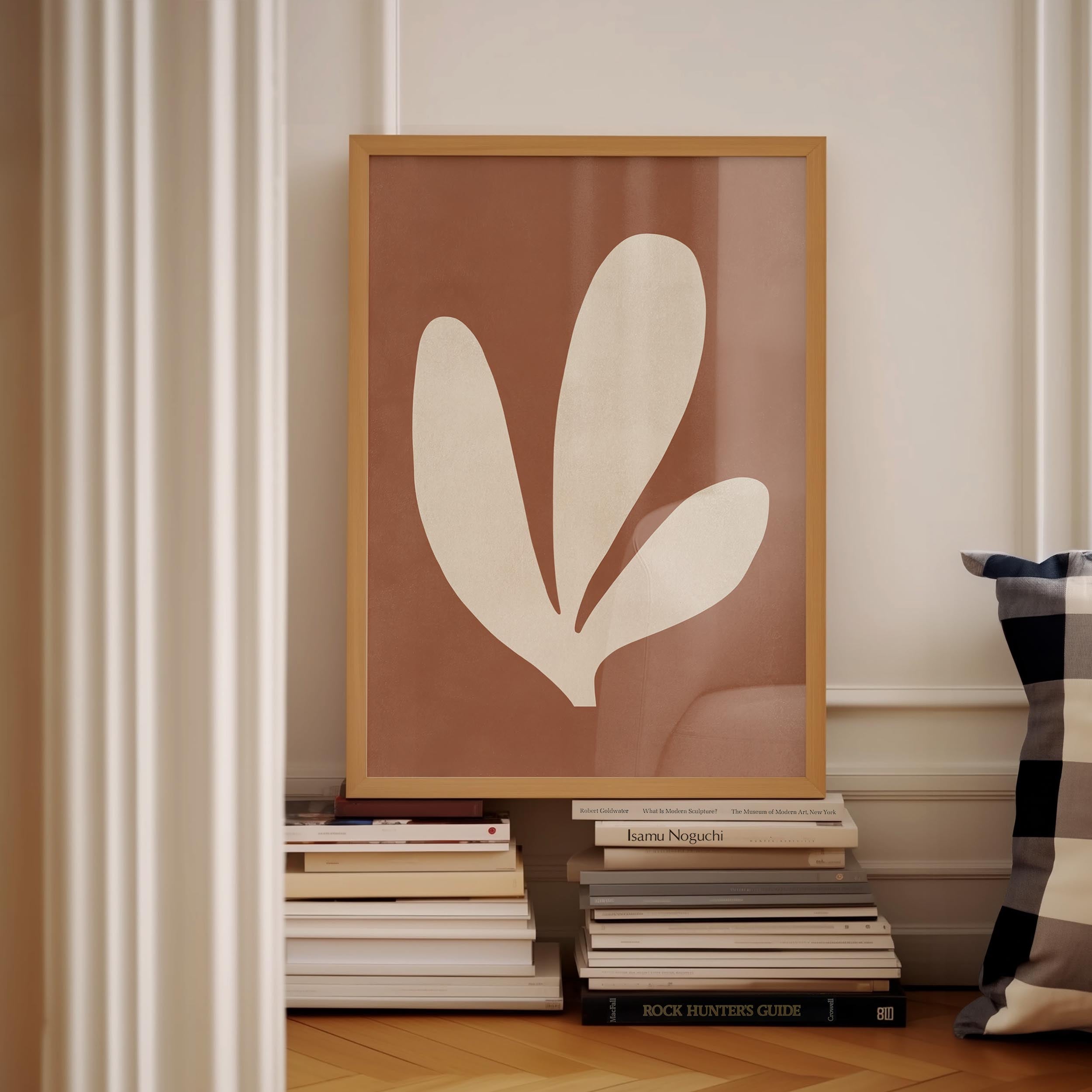 a framed artwork of a leaf-like shape, placed on a shelf among a stack of books.