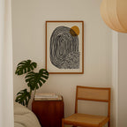 a minimalist interior design with a framed abstract artwork hanging on the wall, a wooden chair, a stack of books, and a potted plant.