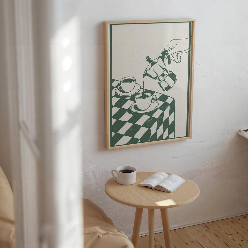 a cozy corner of a room with a wooden table, a white mug, and an open book, all set against a white wall with a framed illustration of a hand pouring coffee.