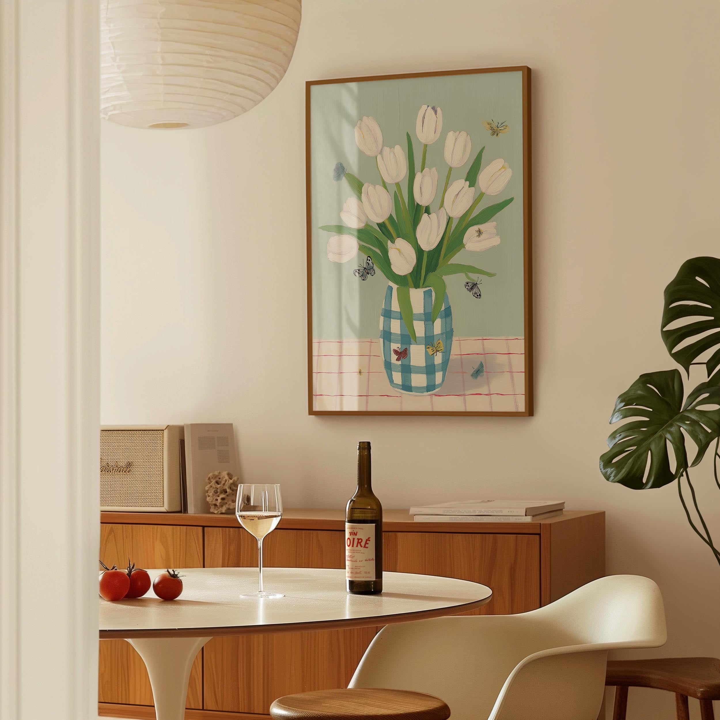 a dining room with a table set for two, a bottle of wine, and a framed painting of white tulips on the wall.