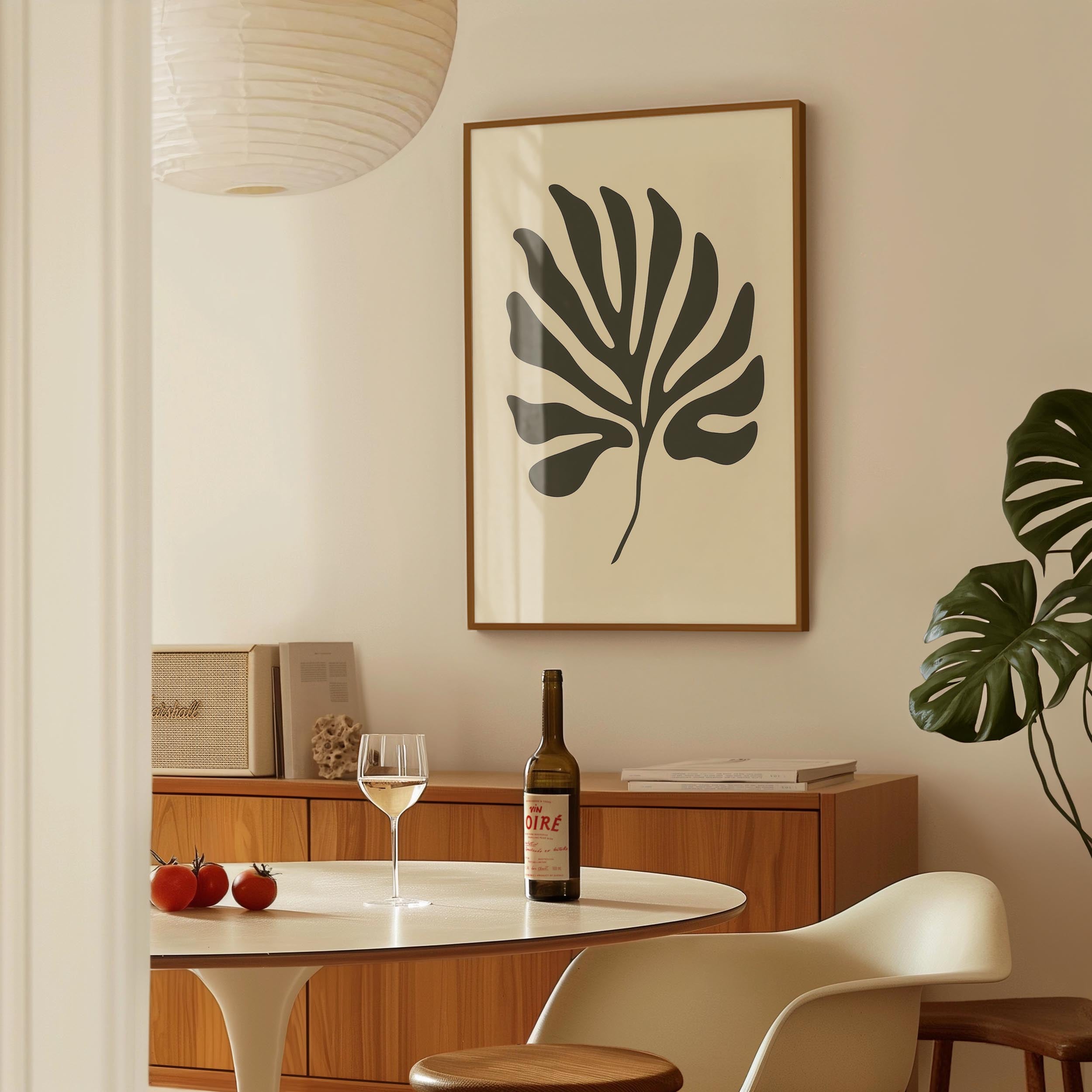 a dining room with a table, a wine bottle, a wine glass, and a framed leaf-shaped artwork on the wall.