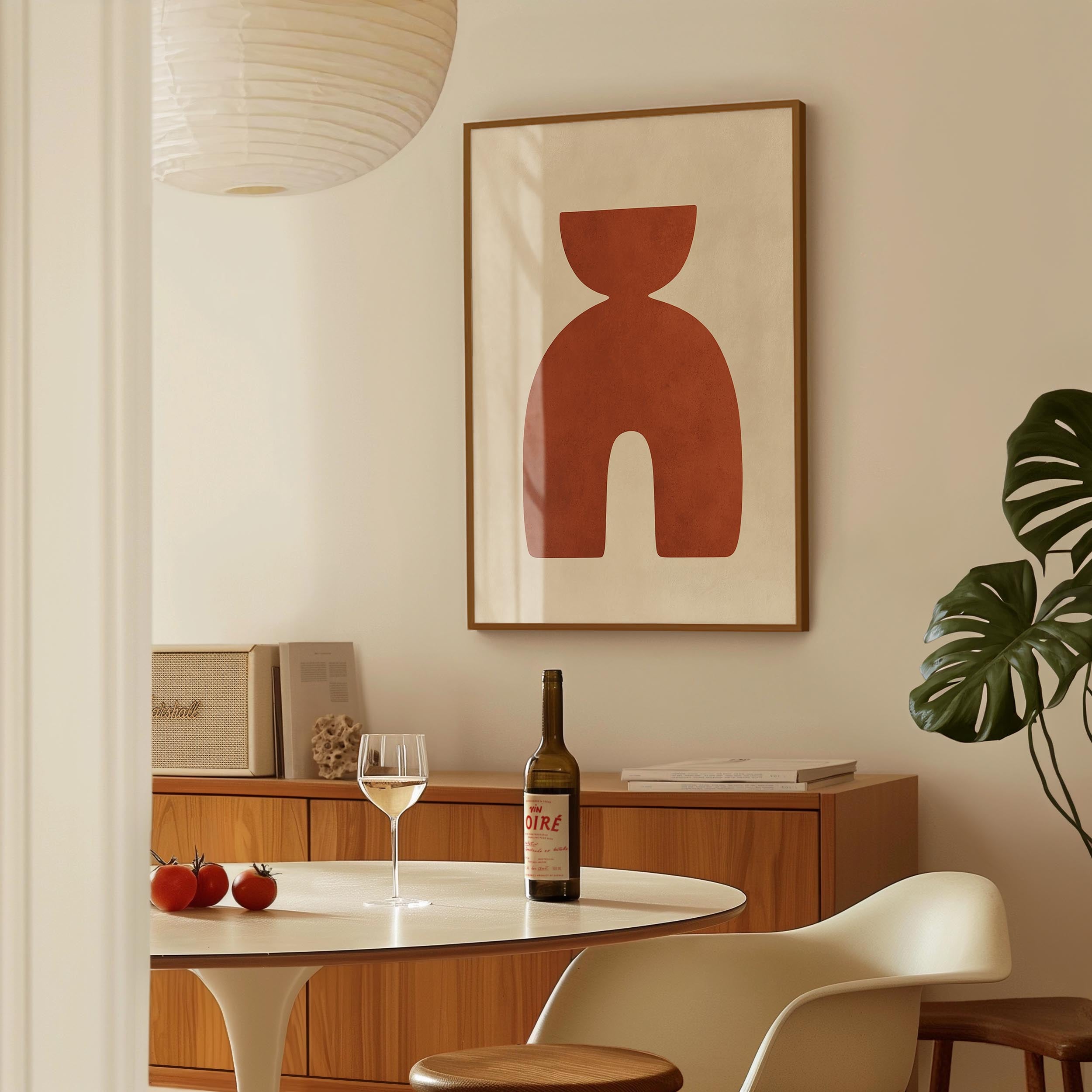 a dining room with a table, a wine bottle, a wine glass, and some fruit. There is a framed abstract artwork hanging on the wall above the table.