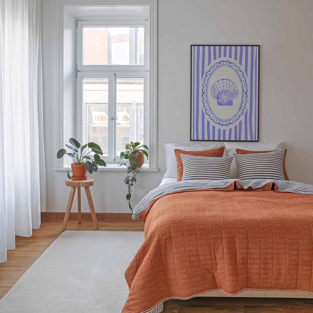 a cozy bedroom with a large bed, a window with a plant on the sill, and a framed artwork featuring a shell design on the wall.