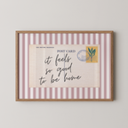 The image is a framed print with a postcard-like design, featuring a handwritten message that reads "it feels so good to be home".