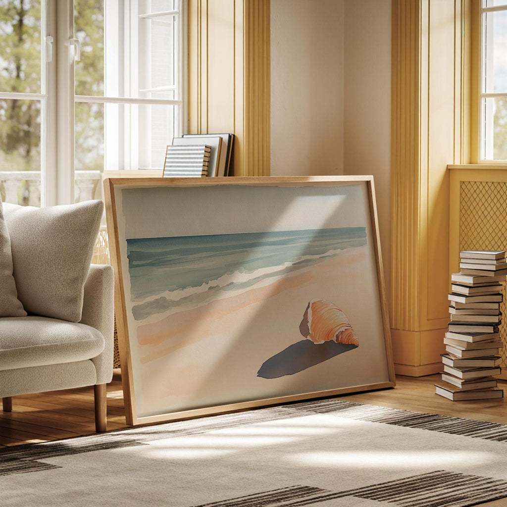 a large framed painting of a beach scene with a shell on the sand, placed on a rug in a room with a window and a stack of books.